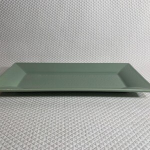 K&ouml;nnte beinhalten: Ein rechteckiger, salbeigr&uuml;ner Servierteller. Das Keramikgeschirr hat einen leicht erh&ouml;hten Rand und eine matte Oberfl&auml;che. Der Teller ist ideal zum Servieren von Vorspeisen oder Desserts. Die Form ist modern und minimalistisch.