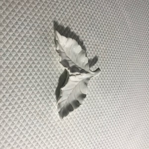 May include: White ceramic leaf-shaped dish with two sections. The dish is designed to look like two leaves joined together at the stem.