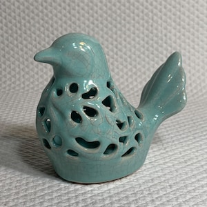 May include: A turquoise ceramic bird figurine with a crackle glaze finish. The bird has cut-out details on its body and a curved tail. This decorative item is suitable for home decor.