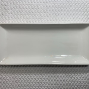 May include: A rectangular white ceramic serving platter. The dish has a smooth, glossy surface and slightly rounded corners. The platter is approximately 12 inches long and 6 inches wide, suitable for serving appetizers or desserts.
