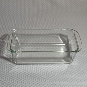 May include: A clear glass loaf pan with rounded edges and handles. The pan is empty and ready for baking.