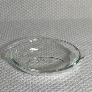May include: A clear glass Pyrex baking dish with two handles. The dish is oval shaped and has a smooth, shiny surface. The Pyrex logo is visible on the bottom of the dish.