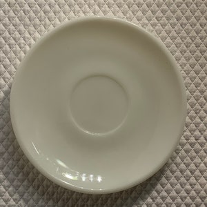 May include: A white ceramic saucer with a slightly raised center.