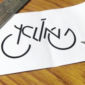 May include: A white piece of paper with the word "cycling" written in black, using the shape of a bicycle.