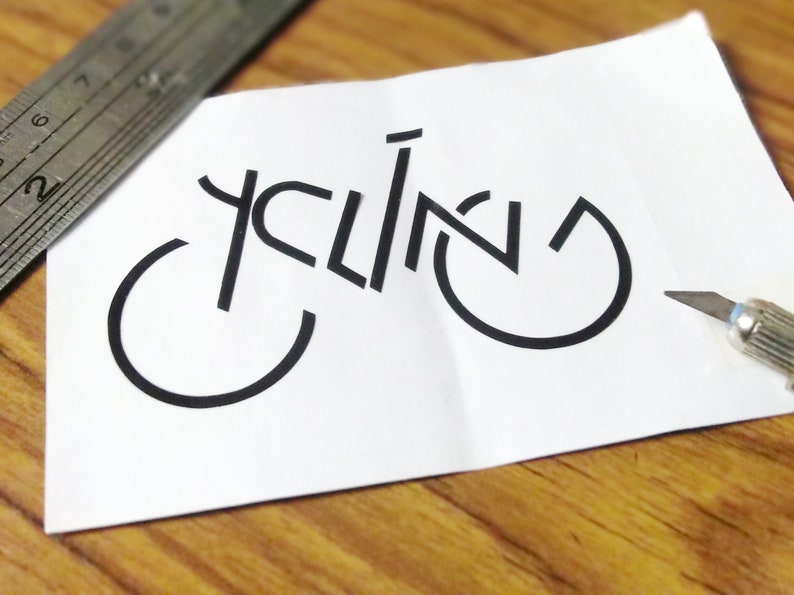 May include: A white piece of paper with the word "cycling" written in black, using the shape of a bicycle.
