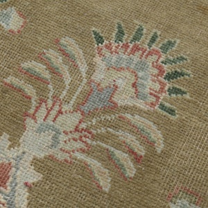 May include: Close-up of a beige rug with a floral pattern. The rug features a design of stylized flowers in shades of pink, green, and blue.