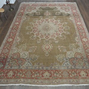 May include: A large, intricately patterned rug with a central medallion in shades of beige, red, and cream. The rug has a border with floral motifs and a fringe edge.