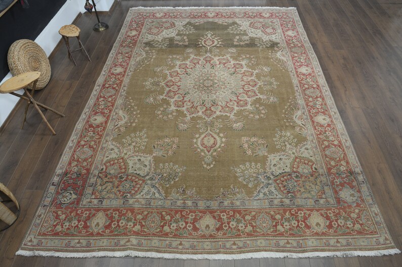 May include: A large, intricately patterned rug with a central medallion in shades of beige, red, and cream. The rug has a border with floral motifs and a fringe edge.