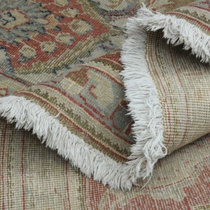 May include: Close-up of a beige and red patterned rug with white fringe. The rug is folded in half, showing the underside of the rug.