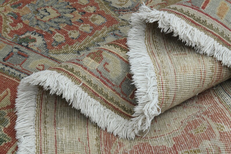 May include: Close-up of a beige and red patterned rug with white fringe. The rug is folded in half, showing the underside of the rug.