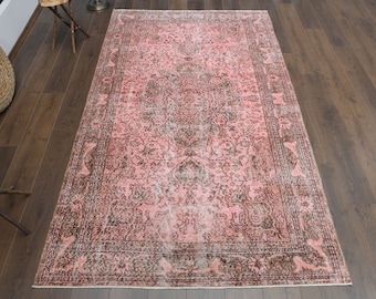May include: A vintage pink and black rug with a floral pattern. The rug has a faded look and a worn border.