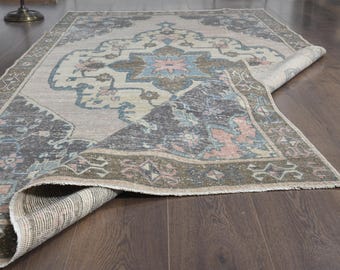 May include: A rectangular rug with a distressed appearance and a rolled edge. The rug has a central medallion design in blue, pink, and beige, with a dark border. It is placed on a dark wood floor.