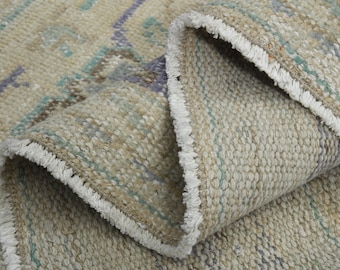 May include: Close-up of a beige rug with a white fringe. The rug has a woven pattern with blue, green, and brown accents.