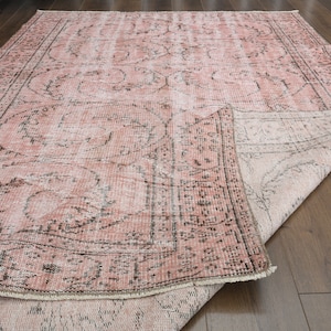 Puede incluir: Una alfombra vintage rosa y blanca con un patrón floral. La alfombra está doblada por la mitad y se ve el revés.