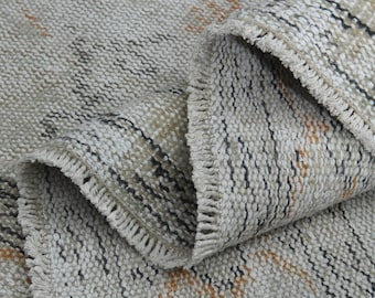 May include: Close-up of a woven rug with a fringe border. The rug has a striped pattern in shades of beige, brown, and black.
