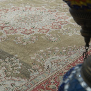 May include: A close-up of a beige rug with a floral pattern. The rug has a central medallion with a repeating pattern of flowers and leaves. The rug is worn and faded, but still beautiful.