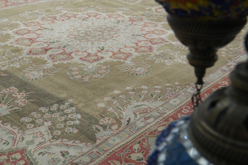 May include: A close-up of a beige rug with a floral pattern. The rug has a central medallion with a repeating pattern of flowers and leaves. The rug is worn and faded, but still beautiful.