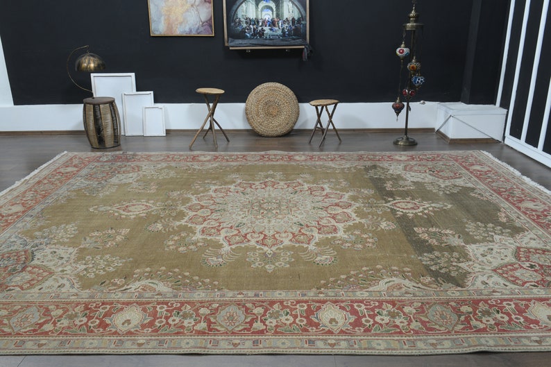May include: A large, intricately patterned rug with a beige background and a central medallion in shades of cream, red, and green. The rug has a red and cream border with floral motifs.