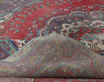 May include: A vintage rug with a red background and intricate floral patterns in shades of blue, pink, and white. The rug is folded in half, revealing the underside, which is a lighter shade of gray with a similar floral pattern.