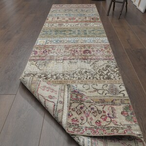 May include: A vintage runner rug with a faded floral pattern in shades of beige, brown, pink, and blue. The rug is rolled up and partially unfurled, revealing the intricate details of the design.