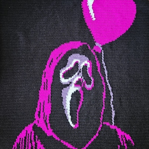 May include: Black crocheted blanket featuring a pink Ghostface design holding a pink heart-shaped balloon. The words "Love You" are written in white above the design. The blanket is a handmade item.