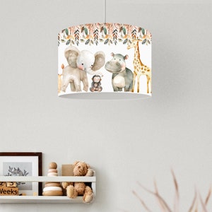 May include: A white lampshade with a watercolour design of jungle animals, including an elephant, monkey, hippo, and giraffe. The top of the lampshade has a decorative border of leaves and branches. The lampshade is suspended from the ceiling.