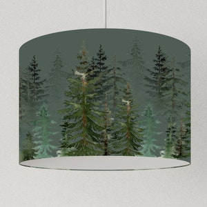 Può includere: Un paralume verde con una stampa ad acquerello di una scena di bosco. Gli alberi sono di vari verdi e marroni, e lo sfondo è di un grigio tenue.