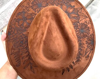 May include: A brown suede fedora hat with a floral design etched into the brim.