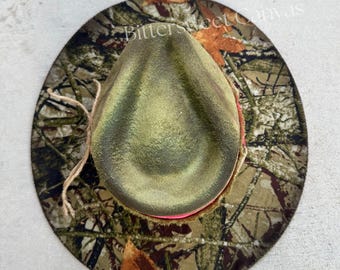 May include: A camouflage print hat with a green crown and a pink interior brim. The hat has a wide brim and a natural rope band. The text "Bittersweet Canvas" is visible on the brim.