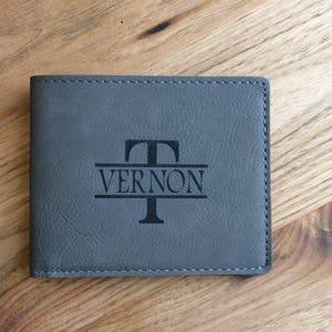 May include: Gray leather wallet with a personalized monogram. The monogram features the letter "T" above the name "VERNON".