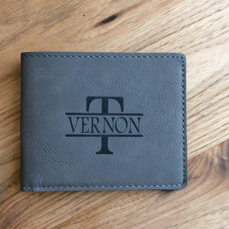 May include: Gray leather wallet with a personalized monogram. The monogram features the letter "T" above the name "VERNON".