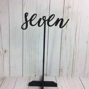 May include: Black wooden table number with the word "seven" in a cursive font.