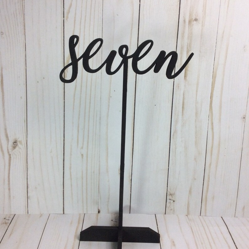 May include: Black wooden table number with the word "seven" in a cursive font.