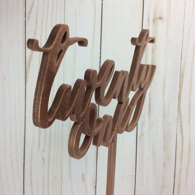 May include: A wooden sign with the words "Twenty One" written in a cursive font. The sign is painted a copper color and is mounted on a wooden stick.