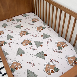 May include: A white cot sheet with a gingerbread house and Christmas tree pattern. The sheet features brown gingerbread houses, green trees, red candy canes, and white snowflakes.