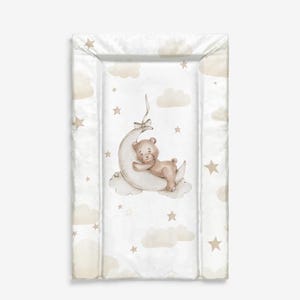 Könnte beinhalten: Eine rechteckige Wickelauflage in sanften, neutralen Farben. Die Auflage zeigt ein skurriles Design eines schlafenden Teddybären auf einem Mond, umgeben von Wolken und Sternen. Das Gesamtthema ist ein Produkt für das Kinderzimmer oder Baby.