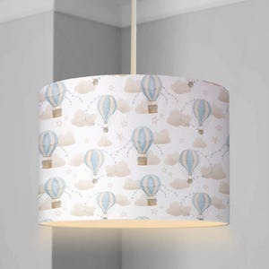 May include: A white lampshade featuring a pattern of blue and white hot air balloons, clouds, and stars. The lampshade is made from fabric and has a white background.