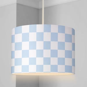 Könnte beinhalten: Zylindrischer Lampenschirm mit hellblauem und weißem Schachbrettmuster. Der Lampenschirm wird von einer weißen Schnur von der Decke abgehängt. Das Licht ist an und beleuchtet die Unterseite des Schirms.