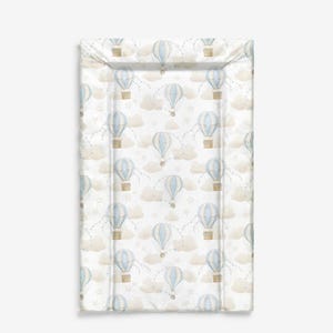 Könnte beinhalten: Eine rechteckige Wickelauflage mit einem sich wiederholenden Muster aus blau-weißen Heißluftballons, Wolken und Sternen auf weißem Hintergrund. Die Ballons haben braune Körbe und sind durch gepunktete Linien verbunden. Die Wolken sind hellbraun.