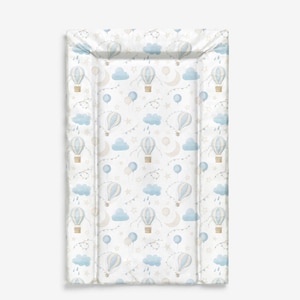 Op de afbeelding: Een rechthoekige aankleedkussen met een patroon van blauwe en witte luchtballonnen, wolken, sterren en manen op een witte achtergrond. De aankleedkussen heeft opstaande randen.