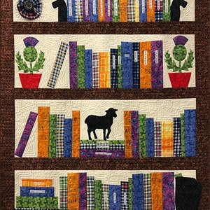 May include: A quilted wall hanging depicting a bookshelf with four shelves. Each shelf is filled with colorful books, and the top and bottom shelves have a black silhouette of a dog. The second and third shelves have a red pot with a green thistle plant. The third shelf also has a black silhouette of a sheep.