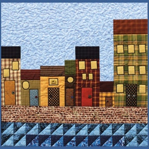 May include: A colorful quilt depicting a row of houses with different patterns and colors. The houses are set against a blue sky with white clouds. The bottom of the quilt features a blue and white geometric pattern.