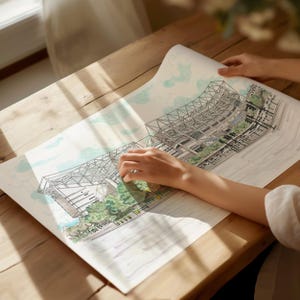 May include: A hand holds a large, detailed drawing of a stadium with a green grassy area and a blue sky. The drawing is on a white sheet of paper.
