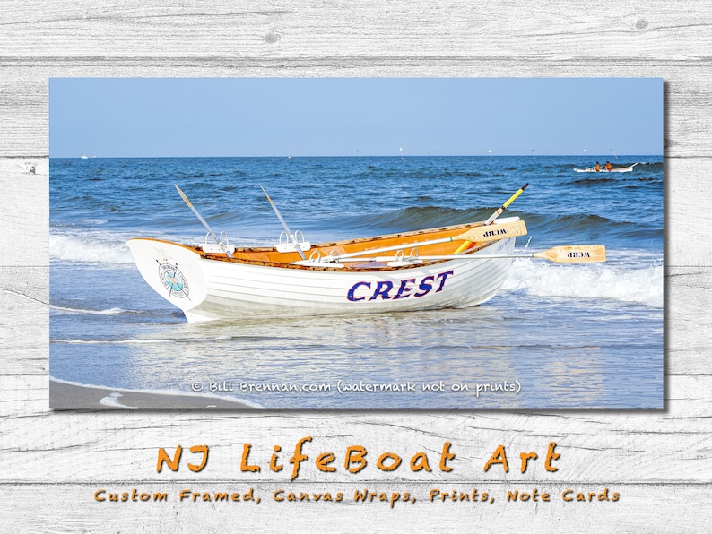 K&ouml;nnte beinhalten: Ein wei&szlig;es und orangefarbenes Holzboot mit der Aufschrift "CREST" liegt an einem Sandstrand mit Meereswellen. Das Boot hat Ruder und ein Kompassdesign. Das Bild ist ein Druck von NJ LifeBoat Art.