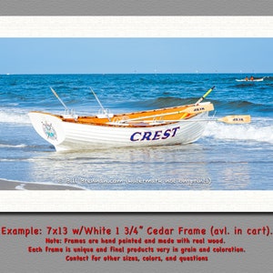 K&ouml;nnte beinhalten: Ein gerahmter Druck mit zwei Ruderbooten am Strand. Das wei&szlig;e Boot im Vordergrund tr&auml;gt das Wort "CREST" in Blau. Die Boote haben orangefarbene Innenr&auml;ume und befinden sich mit Rudern im Wasser. Der Rahmen ist wei&szlig;.