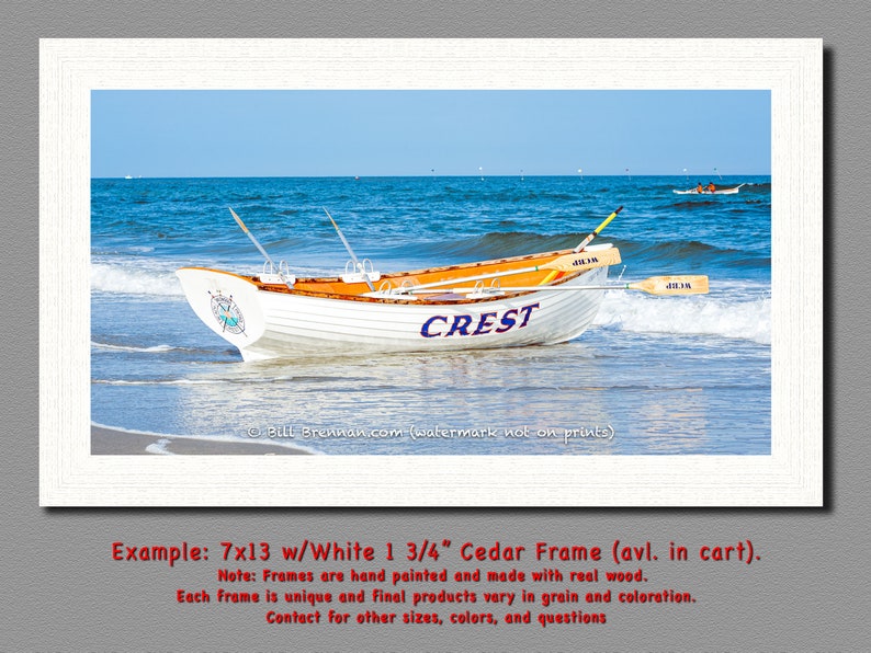 K&ouml;nnte beinhalten: Ein gerahmter Druck mit zwei Ruderbooten am Strand. Das wei&szlig;e Boot im Vordergrund tr&auml;gt das Wort "CREST" in Blau. Die Boote haben orangefarbene Innenr&auml;ume und befinden sich mit Rudern im Wasser. Der Rahmen ist wei&szlig;.