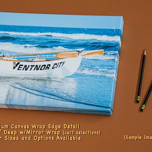 May include: Canvas print of a white rowboat on a beach with the words "VENTNOR CITY" on the side. The ocean is in the background. Two pencils are on the right. The canvas is 1 1/2 inches deep. The text says "Premium Canvas Wrap Edge Detail".