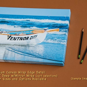 May include: A canvas print depicting a white rowboat on a beach, with the text "VENTNOR CITY". The background shows ocean waves. Two pencils are positioned on the right side of the image.