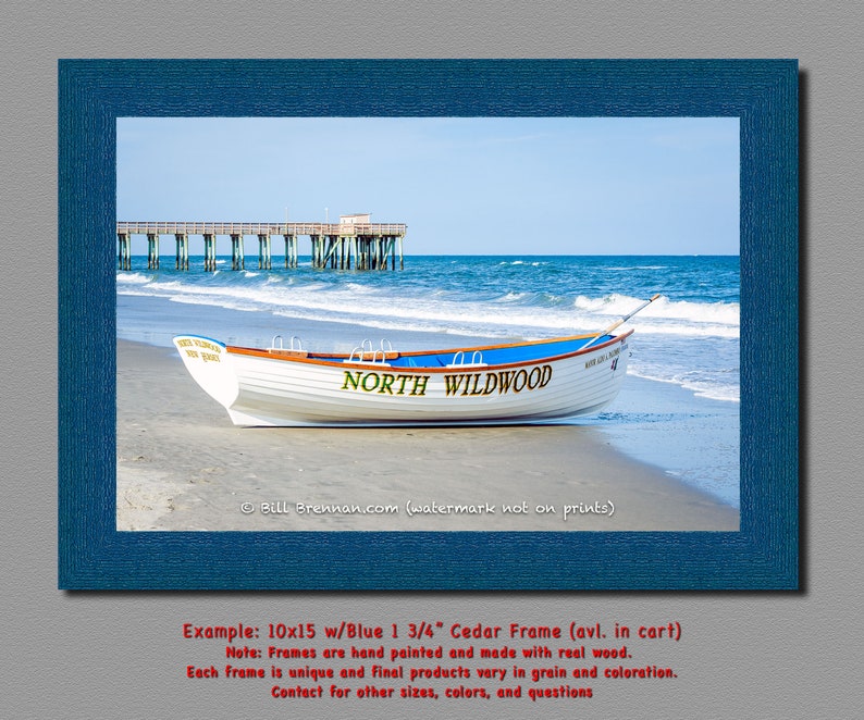 May include: A framed print showing a white boat on a sandy beach with the text "NORTH WILDWOOD". The boat has a blue stripe and is near the sea with a pier in the background. The frame is blue.