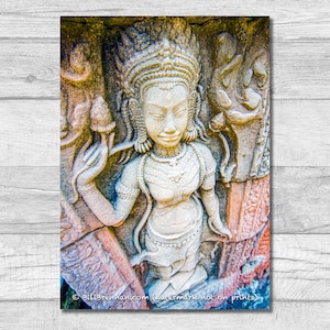 May include: A detailed stone carving of a serene female figure, adorned with an elaborate headdress and jewelry. The figure holds an object in one hand and is surrounded by intricate relief details. The artwork is in shades of beige, tan, and orange.